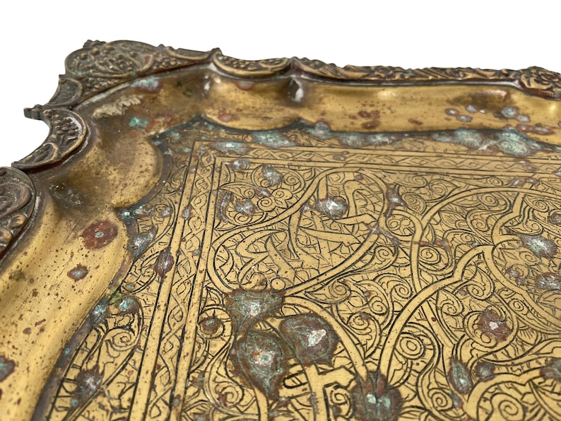 Puede incluir: Una bandeja de metal dorado con un dise&ntilde;o grabado intrincado. La bandeja tiene un borde festoneado y est&aacute; decorada con motivos florales y geom&eacute;tricos.