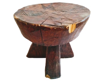 May include: A dark brown wooden stool with a round top and three legs. The top of the stool has a carved design.