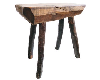 Puede incluir: Un taburete de madera rústico con una tapa rectangular y cuatro patas hechas de ramas naturales. El taburete está hecho de madera marrón oscura y tiene un aspecto áspero y sin terminar.