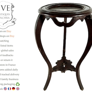 May include: A dark brown wooden plant stand with a round top and three legs. The stand has a decorative design on the bottom.