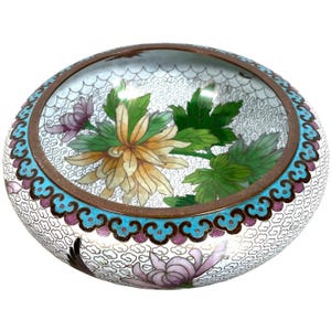 Peut inclure: Un bol en cloisonné blanc avec un motif floral. Le bol est décoré d'une grande fleur de chrysanthème jaune, de feuilles vertes et de fleurs roses. Le bol a une bordure bleue et blanche.