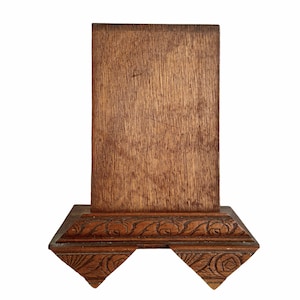 May include: A wooden display stand with a rectangular top and a carved base. The stand is made of dark brown wood and has a natural finish.