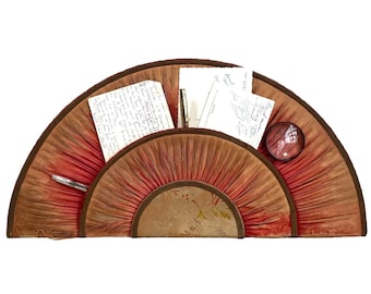 Könnte beinhalten: Ein fächerförmiger Schreibtisch-Organizer in Rot- und Brauntönen mit dunkelbraunem Rand. Er enthält Schreibwaren, einen Stift und eine Lupe. Der Organizer hat eine Vintage-Ästhetik, ideal für ein Homeoffice oder einen Schreibtisch.