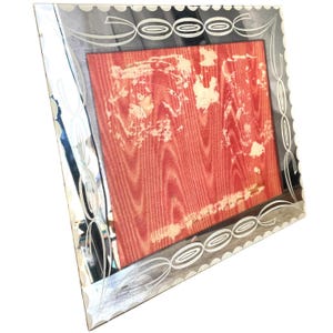 May include: A silver framed mirror with a decorative design of interlocking circles and swirls. The mirror has a red backing.