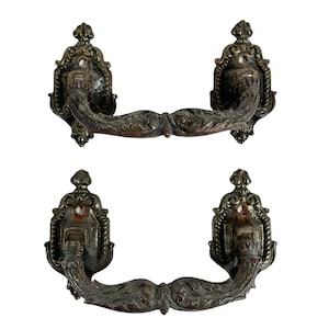 Puede incluir: Dos tiradores de puerta de estilo antiguo, de latón, con un diseño decorativo de volutas. Los tiradores tienen un acabado desgastado con un aspecto usado y envejecido.