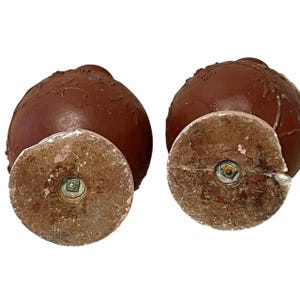 Pu&ograve; includere: Due piedini per mobili decorativi marroni antichi con base rotonda e vite al centro. I piedini hanno una superficie strutturata e sono probabilmente in legno o materiale simile. Le basi sono marrone chiaro con accenti rosa.