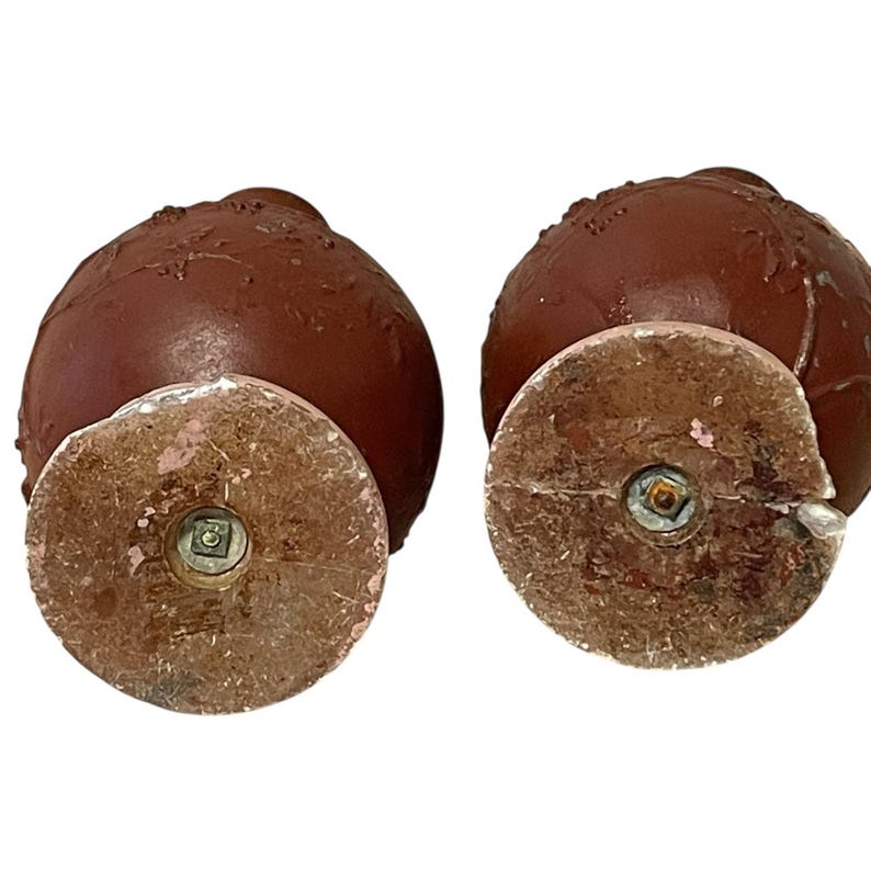 Pu&ograve; includere: Due piedini per mobili decorativi marroni antichi con base rotonda e vite al centro. I piedini hanno una superficie strutturata e sono probabilmente in legno o materiale simile. Le basi sono marrone chiaro con accenti rosa.
