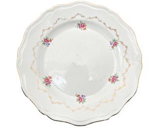 May include: A white porcelain plate with a scalloped edge and a gold trim. The plate is decorated with a floral pattern of pink, red, and blue flowers.