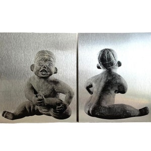 May include: Two grey ceramic sculptures of children sitting on a silver background. The sculpture on the left is of a child sitting with their legs crossed and holding their foot. The sculpture on the right is of a child sitting with their legs crossed and their hands on their hips.