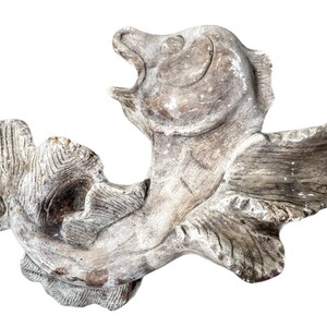 May include: A white, carved, wooden fish sculpture with detailed fins and scales. The fish is curled into a C shape with its mouth open.