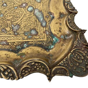 Puede incluir: Una bandeja de metal de color dorado con un dise&ntilde;o grabado intrincado. La bandeja tiene un borde festoneado y est&aacute; decorada con motivos florales y geom&eacute;tricos. La bandeja muestra signos de edad y desgaste, con algunas &aacute;reas de deslustre y p&aacute;tina.