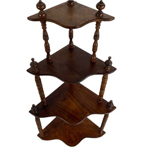 May include: A three-tiered corner shelf made of dark wood with a decorative, turned spindle design. Each shelf has a scalloped edge and the shelf is finished with a dark wood stain.