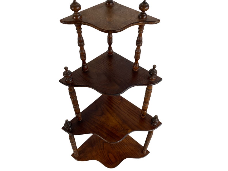 May include: A three-tiered corner shelf made of dark wood with a decorative, turned spindle design. Each shelf has a scalloped edge and the shelf is finished with a dark wood stain.