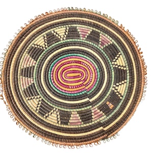 Puede incluir: Una cesta redonda tejida con un patrón marrón, beige y verde. La cesta tiene una franja decorativa alrededor del borde.
