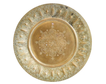 May include: A round, gold-colored metal plate with intricate floral designs etched into the surface. The plate has a raised rim and a smooth, polished center.