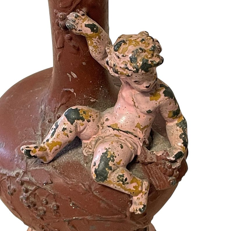 Pu&ograve; includere: Un vaso vintage marrone-rossastro con una statuina di cherubino. Il cherubino &egrave; dipinto di rosa e oro, con aree di perdita di vernice. Il vaso ha una base bulbosa e un collo sottile, con dettagli a rilievo di foglie e uva.