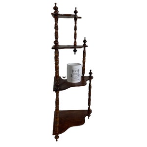 May include: A dark brown wooden corner shelf unit with three shelves. The shelf has decorative turned spindles and a white ceramic mug with the text "EVE" on it.
