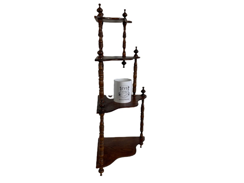 May include: A dark brown wooden corner shelf unit with three shelves. The shelf has decorative turned spindles and a white ceramic mug with the text "EVE" on it.