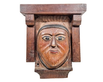 May include: A carved wooden face with painted eyes and lips, framed in a wooden box. The face is a traditional folk art design.