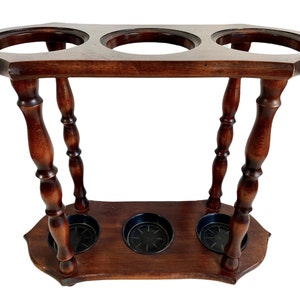 May include: A wooden umbrella stand with three round openings and turned legs. The stand is dark brown and has a slightly curved top.