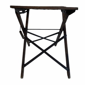 May include: A dark brown wooden folding table with black metal supports. The table is in a folded position, with the legs crossed.