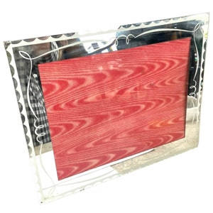 May include: A silver-toned picture frame with a decorative etched design. The frame has a scalloped edge and a red backing.