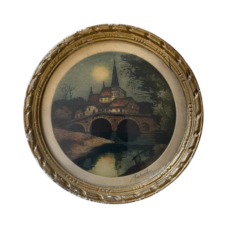 Puede incluir: Una impresi&oacute;n enmarcada de un paisaje nocturno con una iglesia, un puente y agua. El marco redondo es dorado con un dise&ntilde;o ornamentado. La obra de arte tiene un formato circular. La impresi&oacute;n muestra una luna llena.