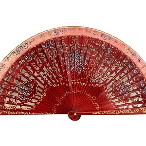 Puede incluir: Un abanico de mano rojo y rosa con detalles dorados y morados. El abanico está decorado con un patrón floral y tiene un mango de madera tallada.