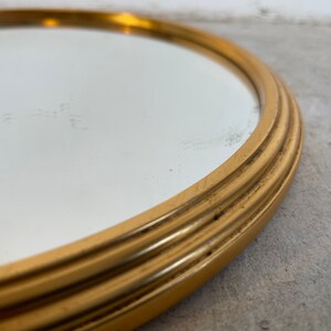 Peut inclure: Un miroir rond avec un cadre dor&eacute;. Le cadre est orn&eacute; d'une s&eacute;rie de cr&ecirc;tes sur&eacute;lev&eacute;es autour du bord.