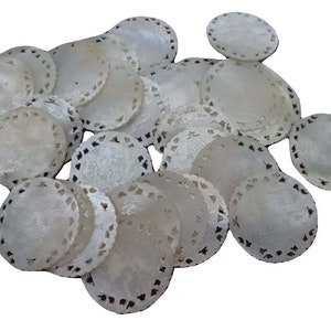 May include: A pile of white, round, decorative coasters made of mother of pearl. The coasters have a delicate, intricate design carved into the surface.