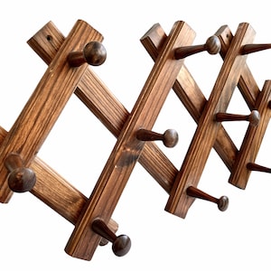 May include: A wooden coat rack with multiple hooks. The rack is made of dark brown wood and has a staggered design. The hooks are made of wood and have a rounded shape.