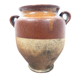 May include: A brown and beige ceramic jar with two handles. The jar has a rustic, vintage look.