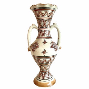 May include: A white ceramic vase with two handles and a geometric pattern in brown and red.