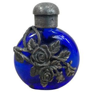 Peut inclure: Un flacon en verre bleu cobalt avec un bouchon en métal argenté et un motif de rose en métal argenté.