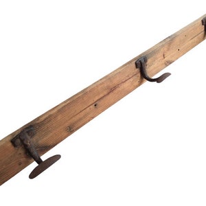 May include: A rustic wooden coat rack with three metal hooks. The rack is made of natural wood with a weathered finish. The hooks are made of black metal and are shaped like a simple curve.