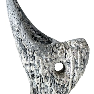 Könnte beinhalten: Eine graue Keramikvase mit einer einzigartigen, organischen Form und einer strukturierten Oberfläche. Die Vase hat ein Loch an der Seite, wodurch sie sich ideal für die Präsentation von Blumen oder anderen Dekorationselementen eignet.
