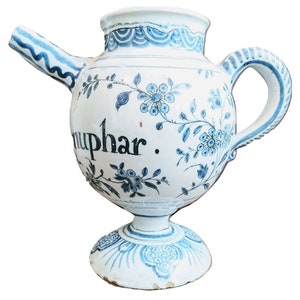 Op de afbeelding: Een witte keramische kan met een blauw en wit bloemenmotief. De kan heeft een tuit en een handvat. Het woord "Nuphar" staat op de zijkant van de kan.