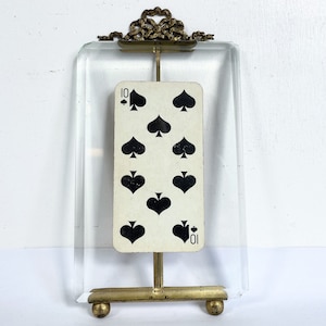May include: A glass picture frame with a gold metal stand and ornate top. The frame holds a playing card, the ten of spades.