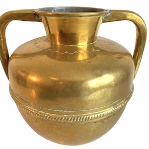 May include: A large, gold-colored brass vase with two handles. The vase has a round body and a wide mouth.