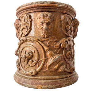 Può includere: Un vaso in ceramica marrone con un design decorativo che presenta un viso grottesco e motivi floreali.