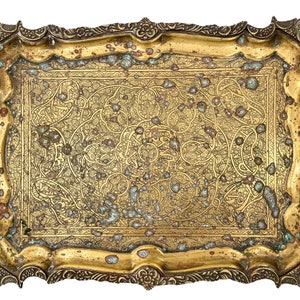 Puede incluir: Una bandeja de metal dorada con un dise&ntilde;o grabado ornamentado. La bandeja tiene una forma rectangular con esquinas redondeadas y un borde elevado.