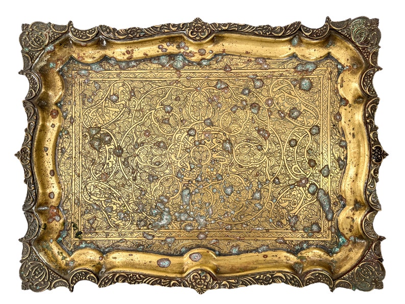 Puede incluir: Una bandeja de metal dorada con un dise&ntilde;o grabado ornamentado. La bandeja tiene una forma rectangular con esquinas redondeadas y un borde elevado.