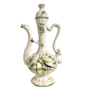 May include: A white ceramic pitcher with a green and yellow floral design and a peacock illustration. The pitcher has a tall, slender neck and a round body. It has a lid with a finial.