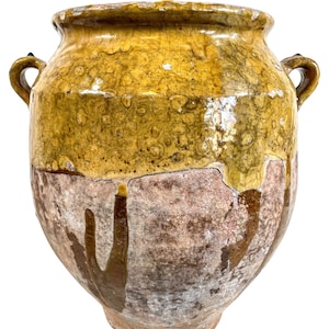 May include: A large, yellow glazed ceramic pot with two handles. The pot has a rustic, aged look with brown and white streaks of glaze.