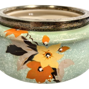 May include: A green ceramic bowl with a silver rim and floral design. The bowl has a speckled glaze and features orange, yellow, and brown flowers. The silver rim is marked "Golay" and "Yoeman Plate."
