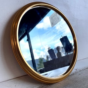 Peut inclure: Un miroir rond avec un cadre dor&eacute; d&eacute;coratif &agrave; bordure multicouche. Le miroir refl&egrave;te un ciel nuageux et l'int&eacute;rieur d'un magasin.
