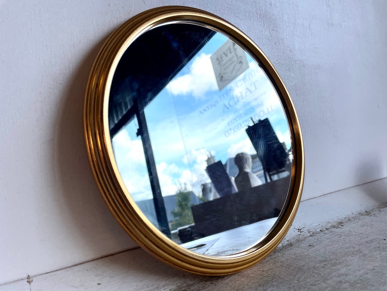 Peut inclure: Un miroir rond avec un cadre dor&eacute; d&eacute;coratif &agrave; bordure multicouche. Le miroir refl&egrave;te un ciel nuageux et l'int&eacute;rieur d'un magasin.