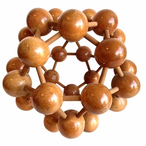 May include: A wooden model of a molecule with a spherical shape. The model is made of many small, round wooden balls connected by wooden sticks. The balls are a light brown color and the sticks are a darker brown color.