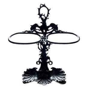 May include: A black metal umbrella stand with two circular rings and a decorative base with a floral design.