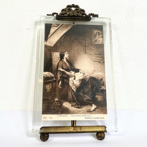 May include: A vintage glass picture frame with a gold metal stand and a black and white photo of a woman and a child. The photo is titled "T.ISSAERT - Une famille malheureuse" and "MUSEE DU LOUVRE, PARIS".